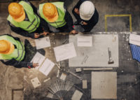 Construction workers in protective gear reviewing blueprints at a table.