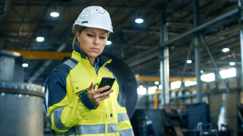 Woman in hard hat and reflective vest using mobile phone